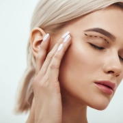 Plastische Chirurgie. Eine schöne junge blonde Frau mit geschlossenen Augen, die ihr Gesicht berührt, auf dem eine Skizze zu sehen ist.