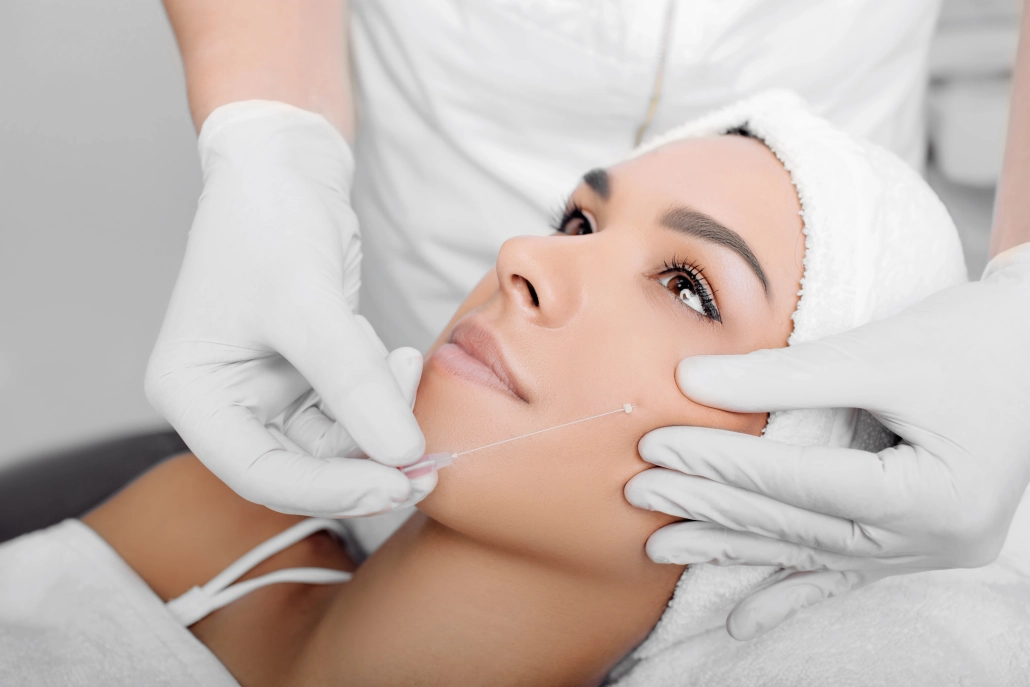 Plastischer Chirurg in weißen Handschuhen führt ein Fadenlifting im Wangenbereich einer Patientin durch Fadenlifting – Minimalinvasive Behandlung zur Hautstraffung im Gesicht